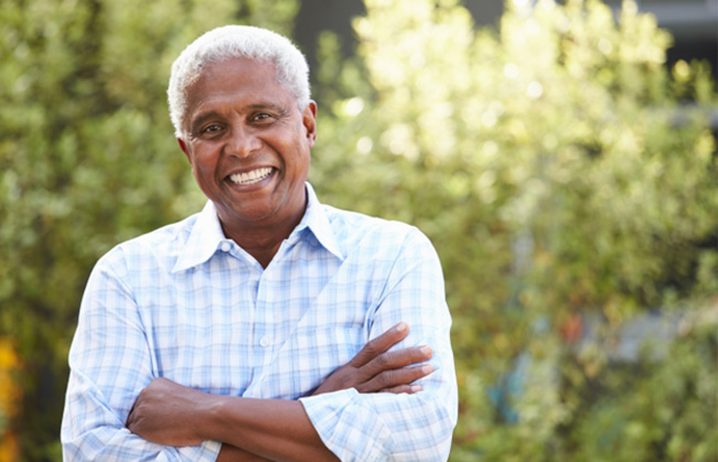 Older man standing outside smiling with arms folded