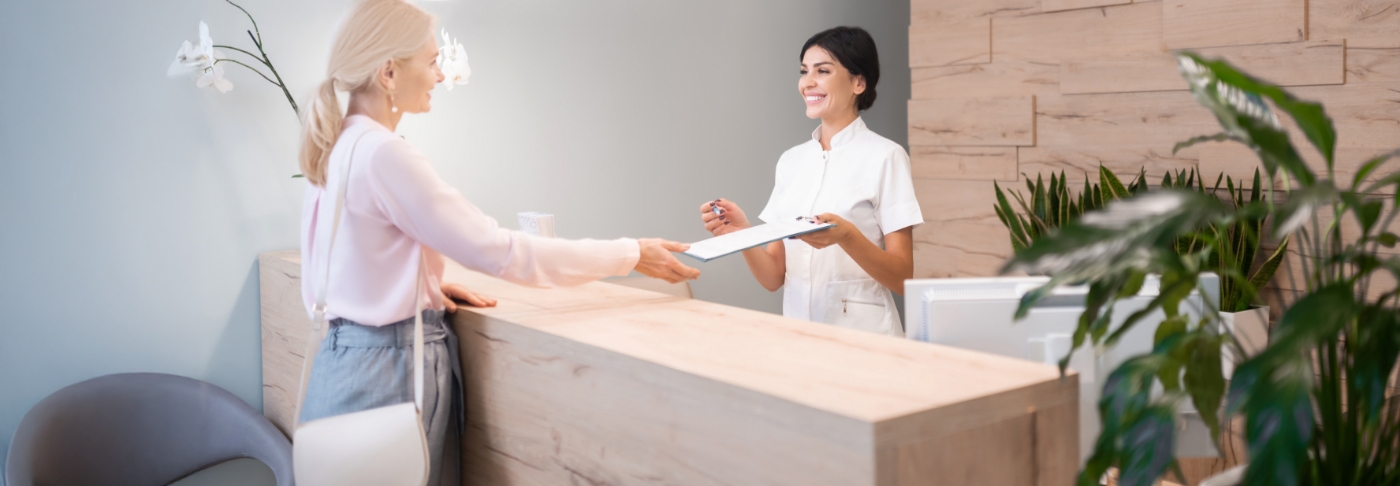 Dental office receptionist handing a clipboard to a patient