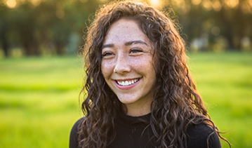 Young woman with long curly brown hair smiling in a park