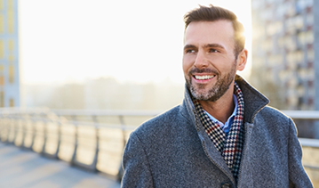 Man in a gray peacoat smiling on a city street